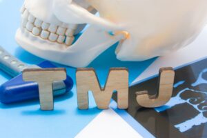 A model skull sits on a table with the letters TMJ in front made from wood.